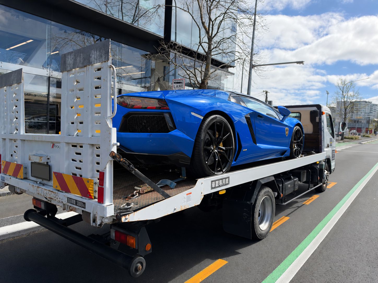Rear side view of the Lamborghini on Drive1's flatbed, with the truck registration covered and the car digitally recoloured blue.